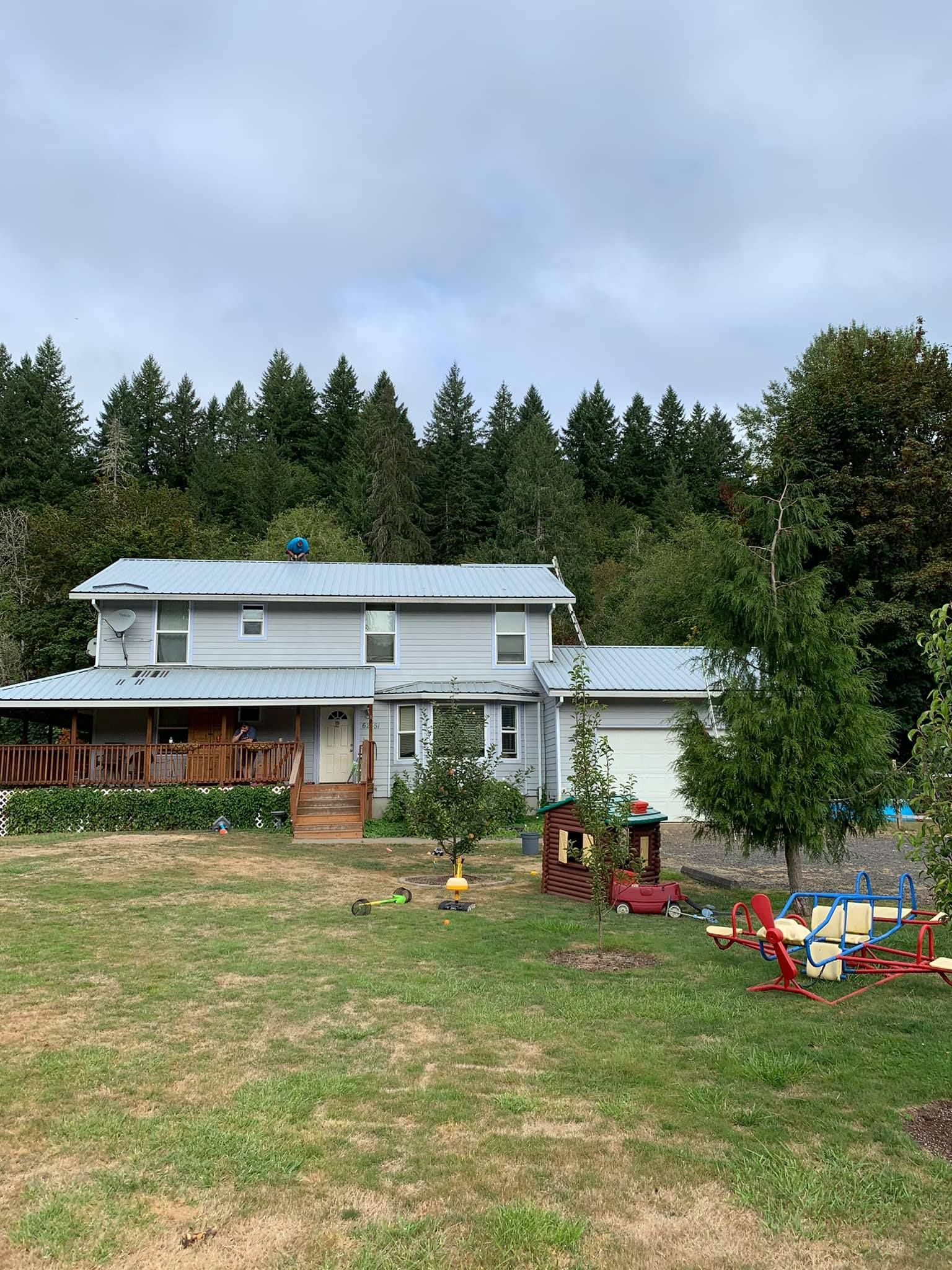 A large house with a metal roof is sitting in the middle of a lush green field surrounded by trees.