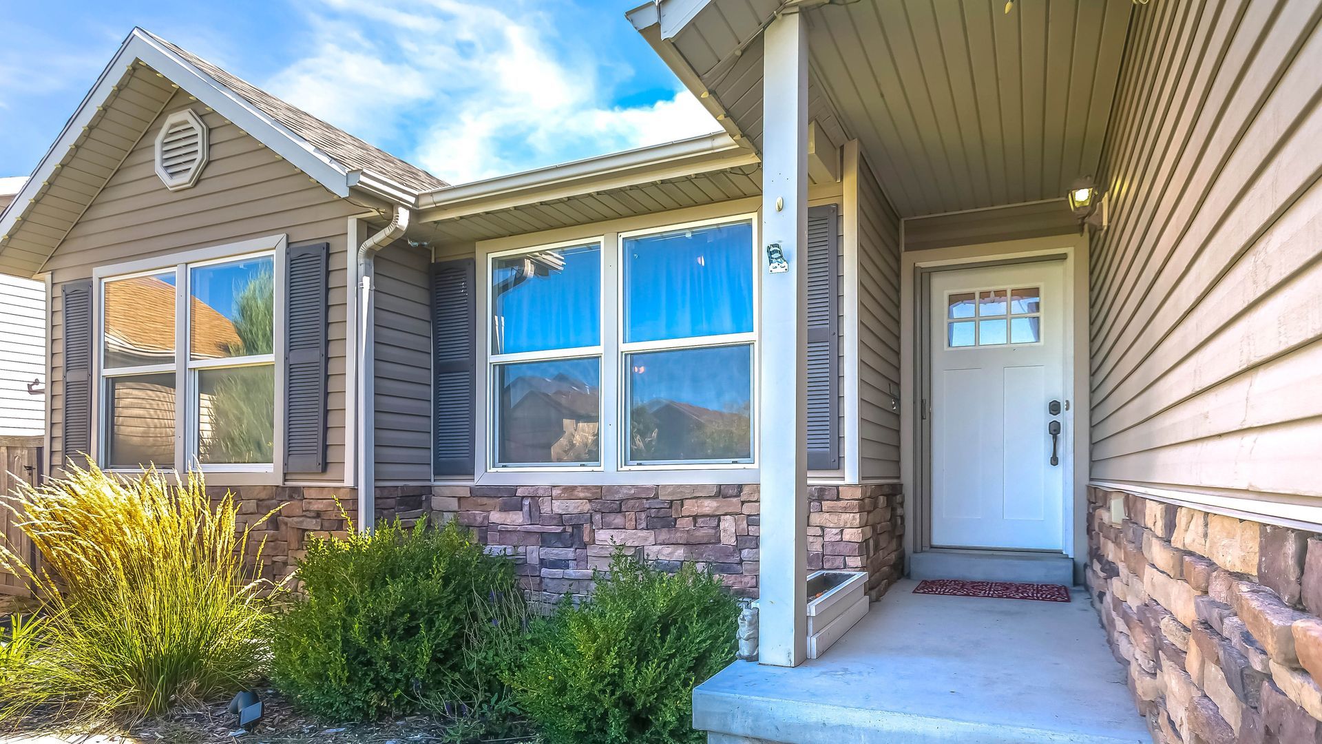 House exterior with brown siding, stone facade, and a white front door under a porch.
