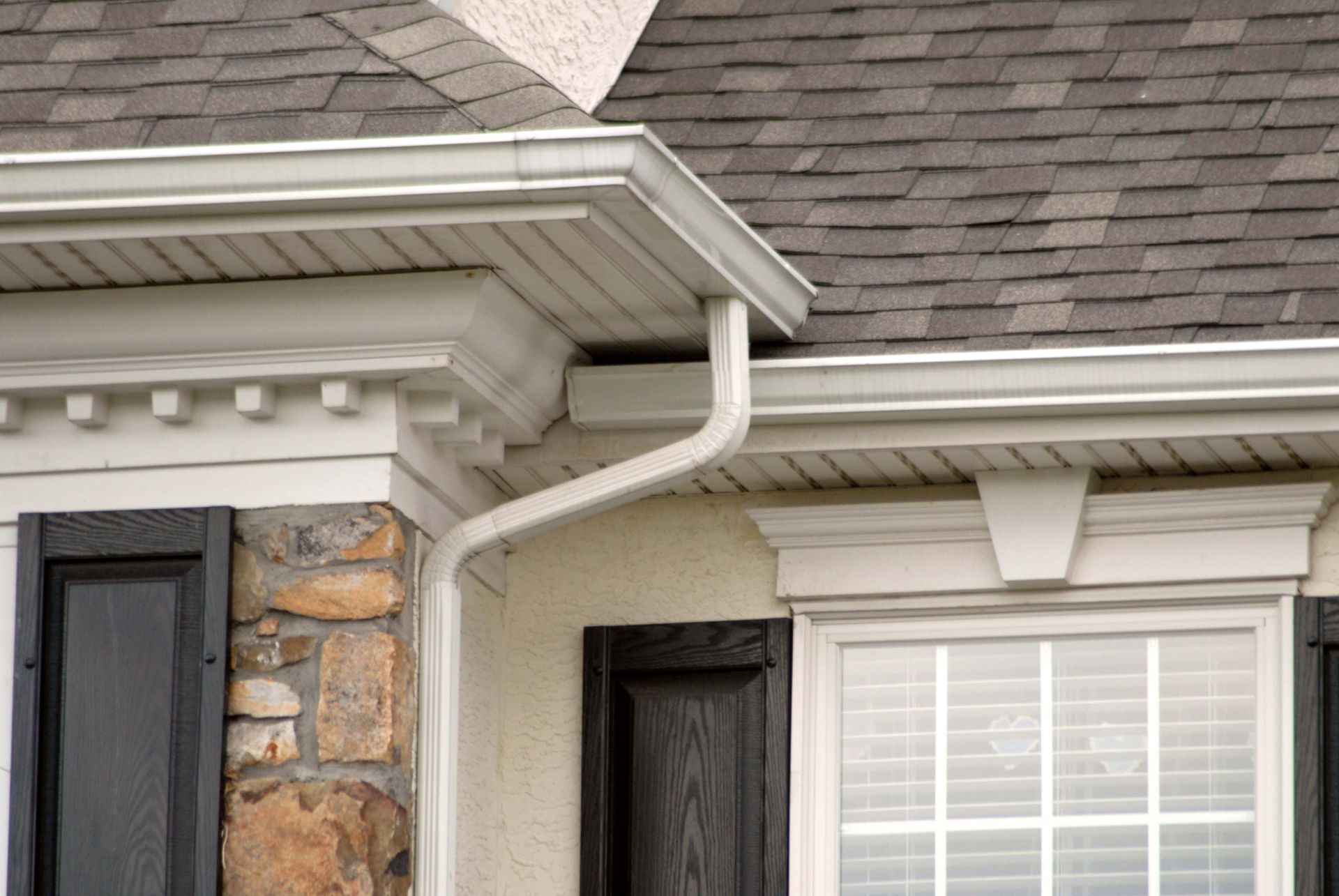 White house rain gutter system.  The downspout is connected to the gutter along the roofline.