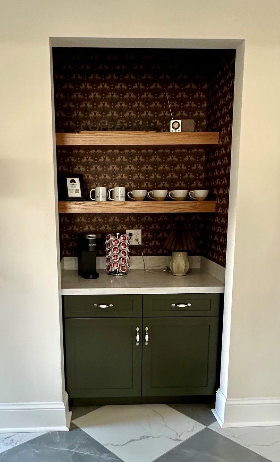 Built-in kitchen nook with dark wallpaper, wooden shelves, and green lower cabinets holding dishes and jars