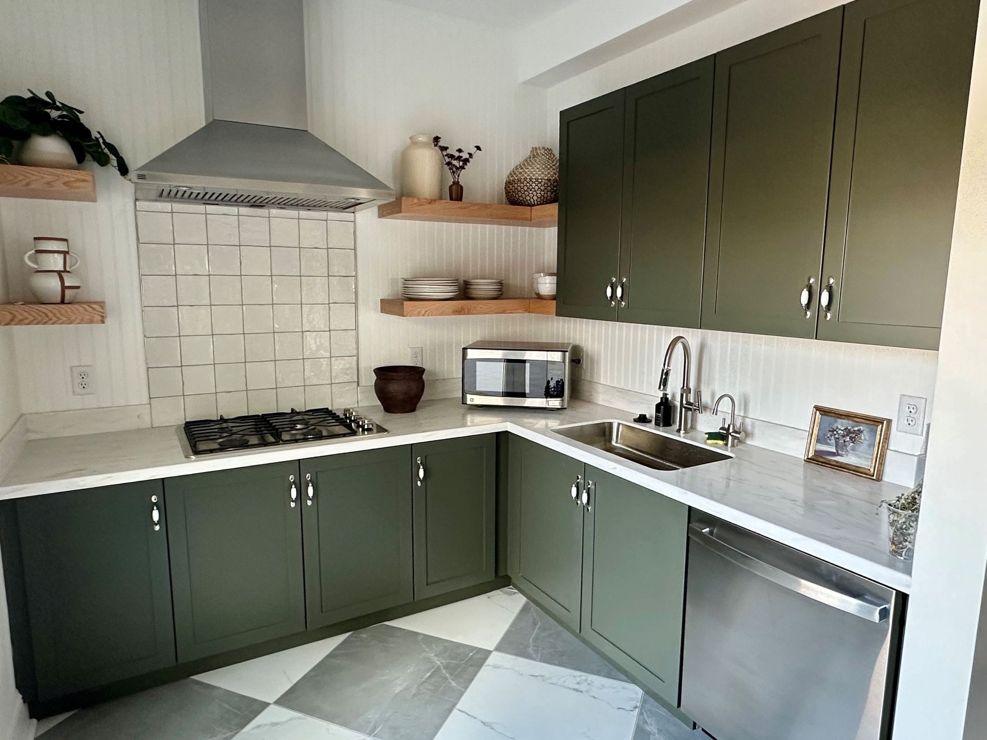 Green kitchen with white tile backsplash, stainless appliances, and wood shelves on gray patterned floor