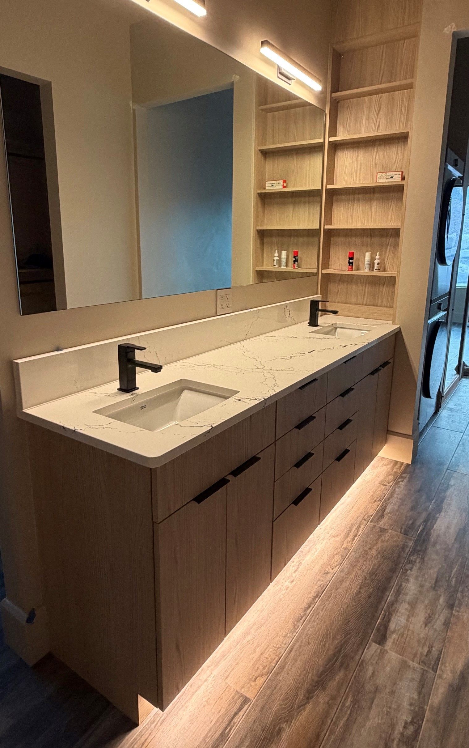 Modern bathroom vanity with double sinks, large mirror, and built-in shelves in warm lighting