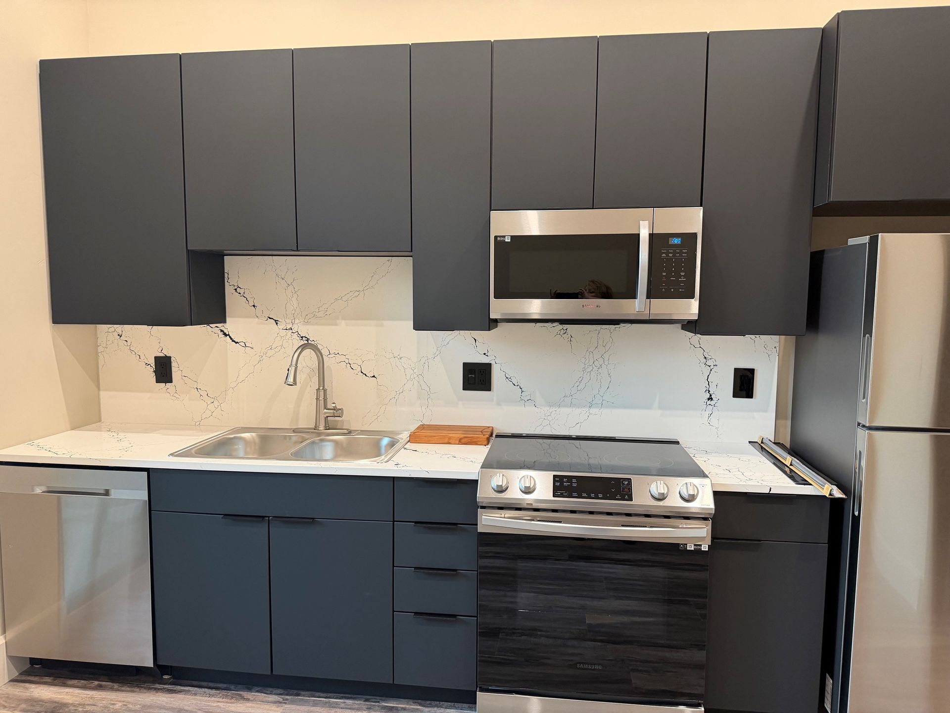 Modern kitchen with dark cabinets, white marble backsplash, stainless appliances, and wood countertops