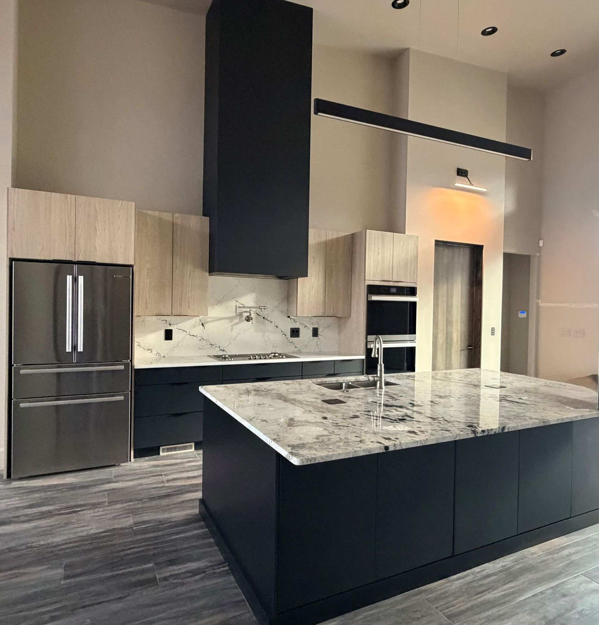 Modern kitchen with dark cabinets, large granite island, stainless appliances, and high ceilings