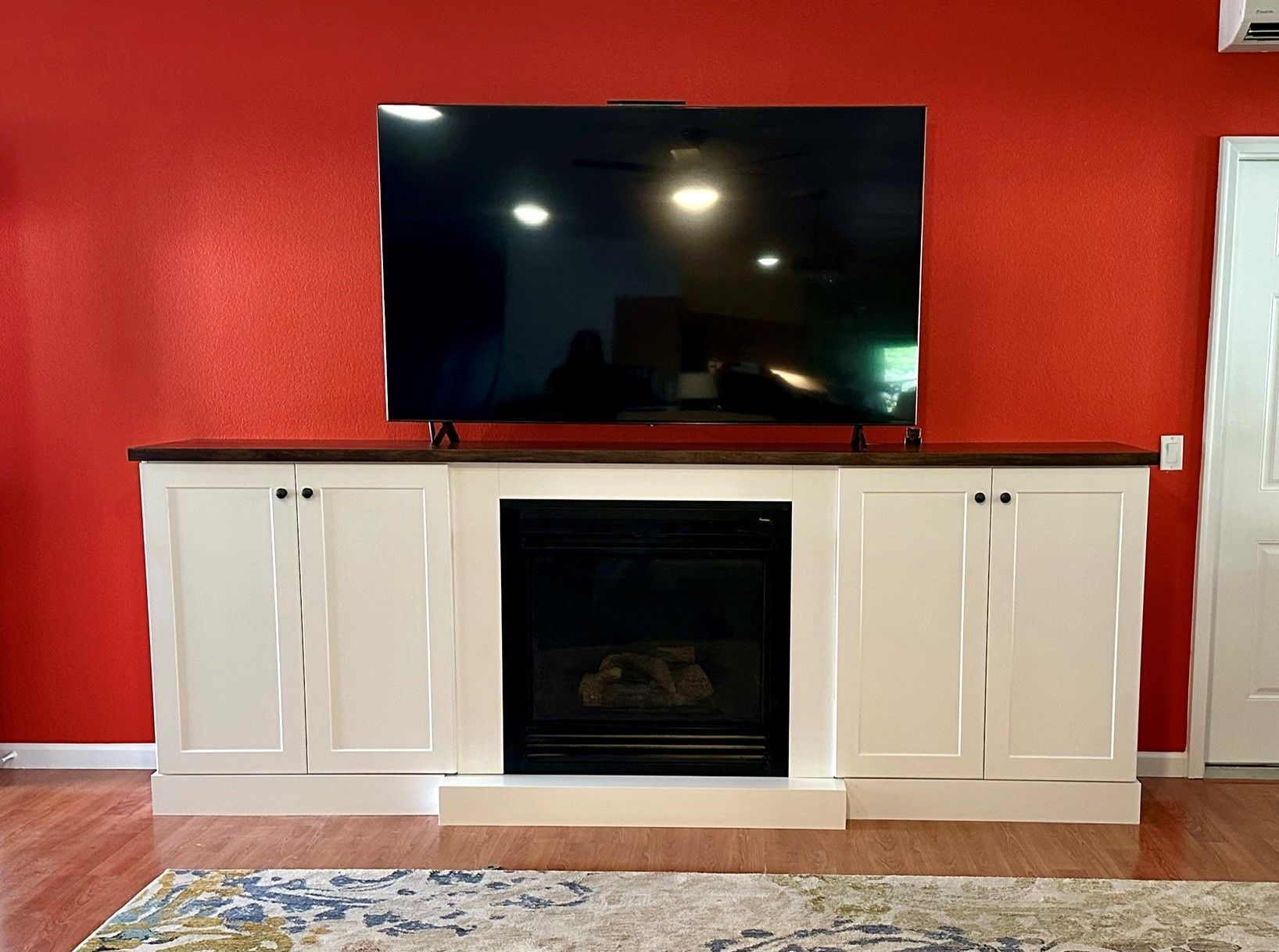 White fireplace console with TV on top against a red wall in a living room.
