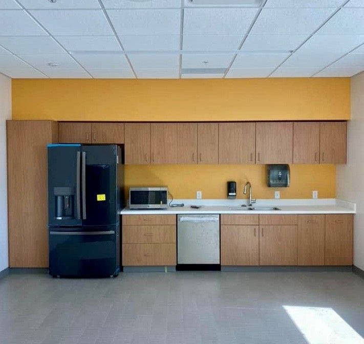 Empty break room kitchenette with black refrigerator, wooden cabinets, yellow wall, and sink counter