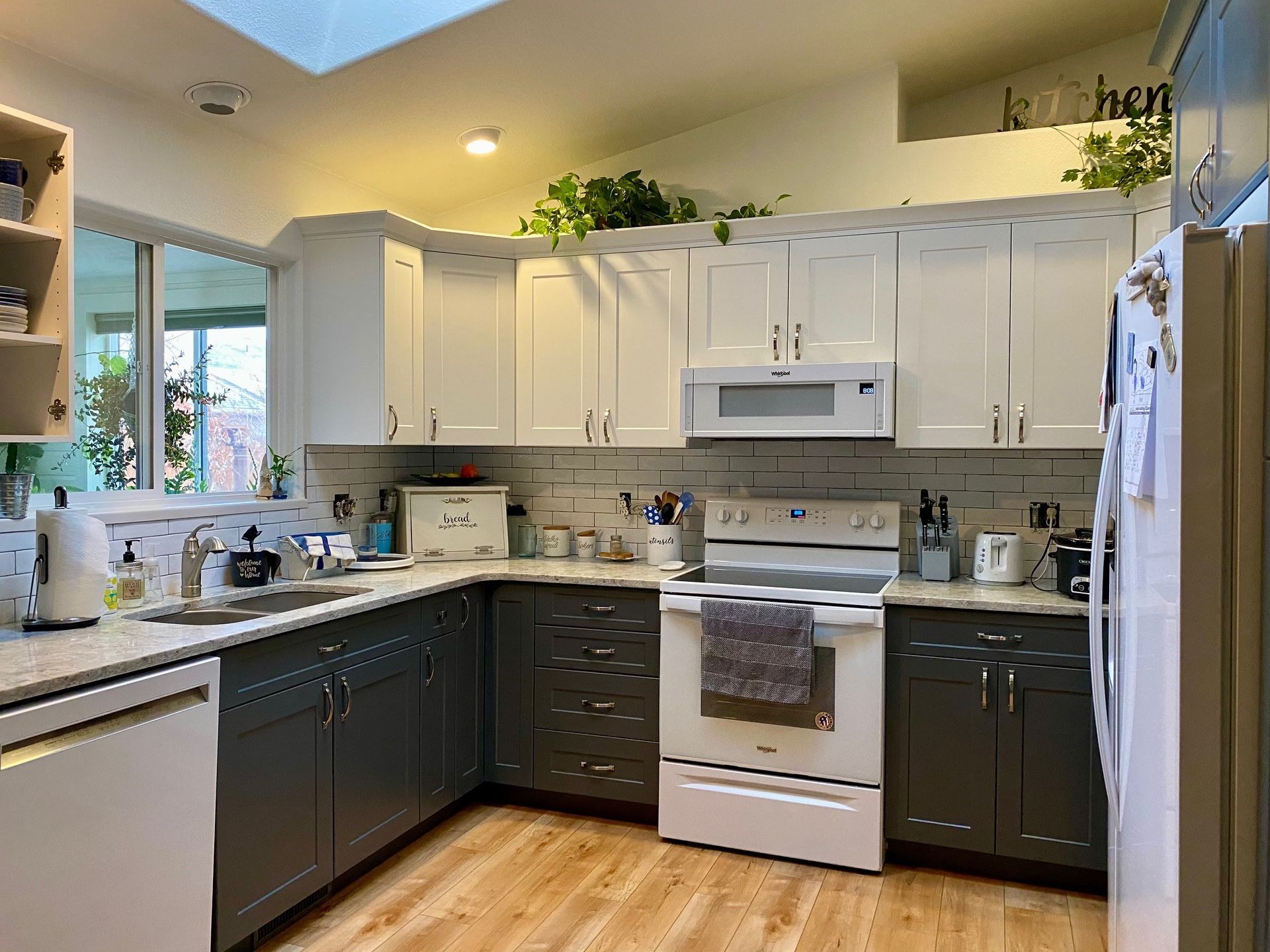 Bright kitchen with white and dark cabinets, white appliances, and a window over the sink