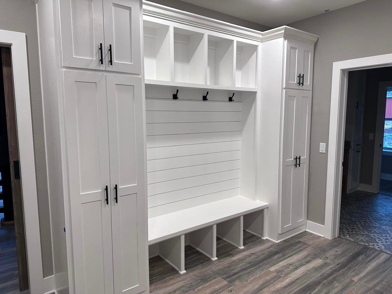 Built-in mudroom bench with white cabinets, cubbies, hooks, and storage cubbies in a gray hallway