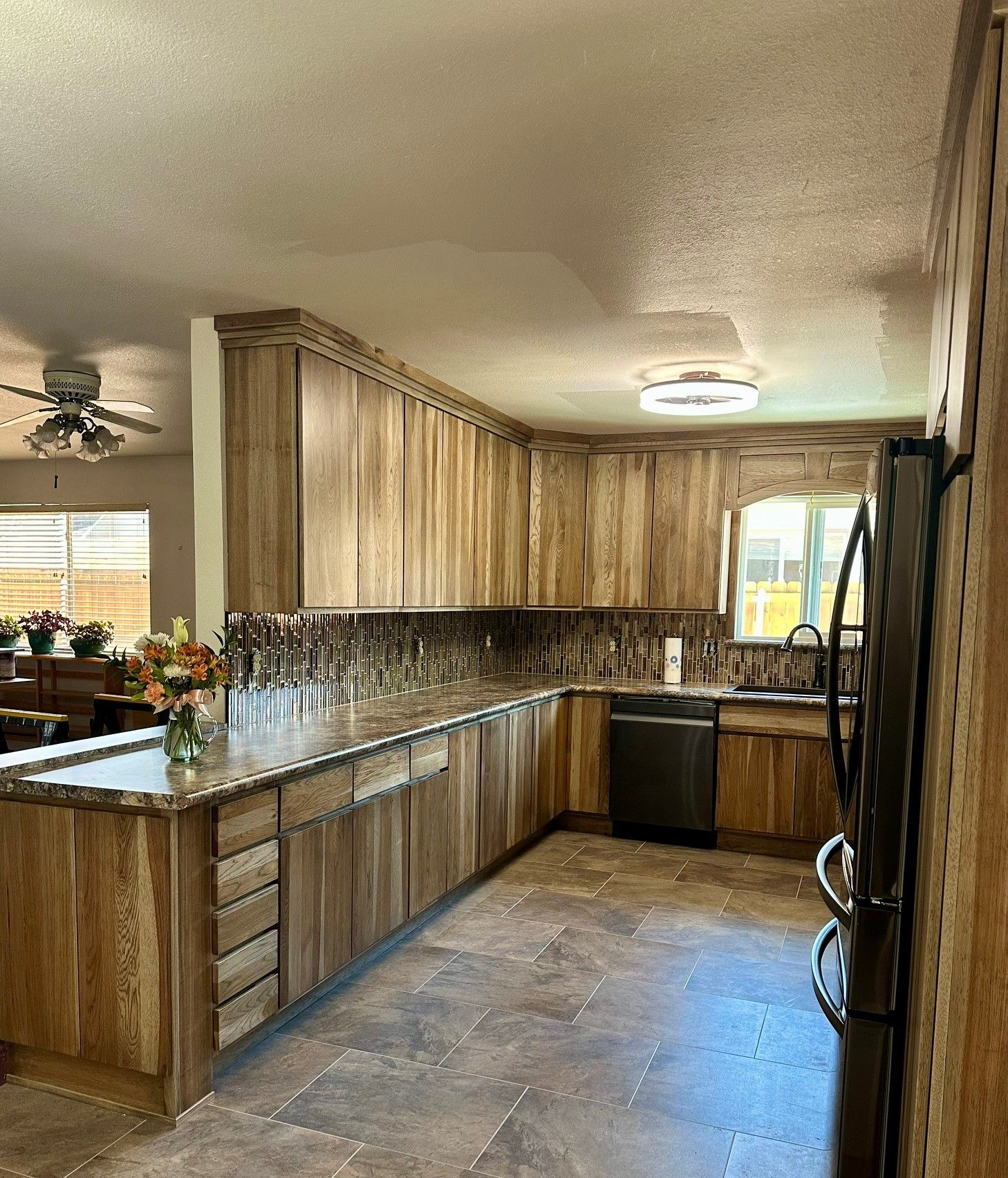 Long kitchen with wood cabinets, dark countertops, island, and a window over the sink.