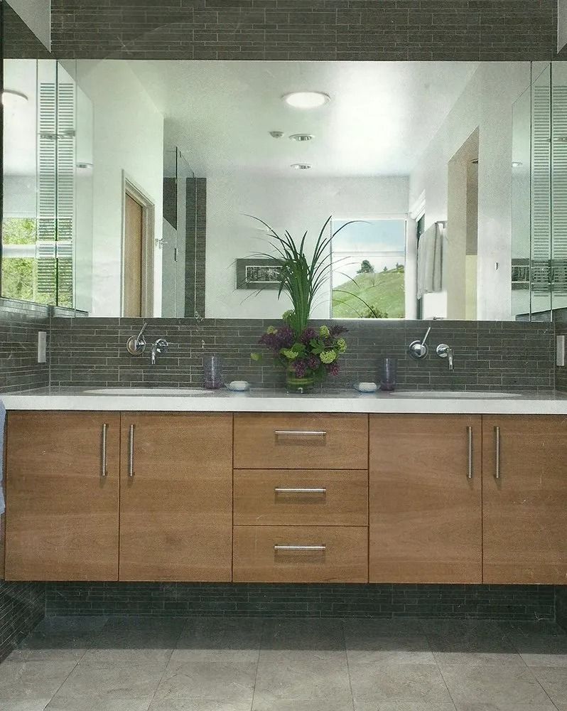 Modern bathroom vanity with wooden cabinets, dark tile backsplash, large mirror, and sink under soft light