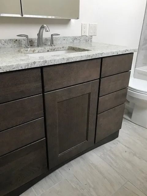 Dark wood bathroom vanity with white granite countertop, sink, faucet, and mirror.