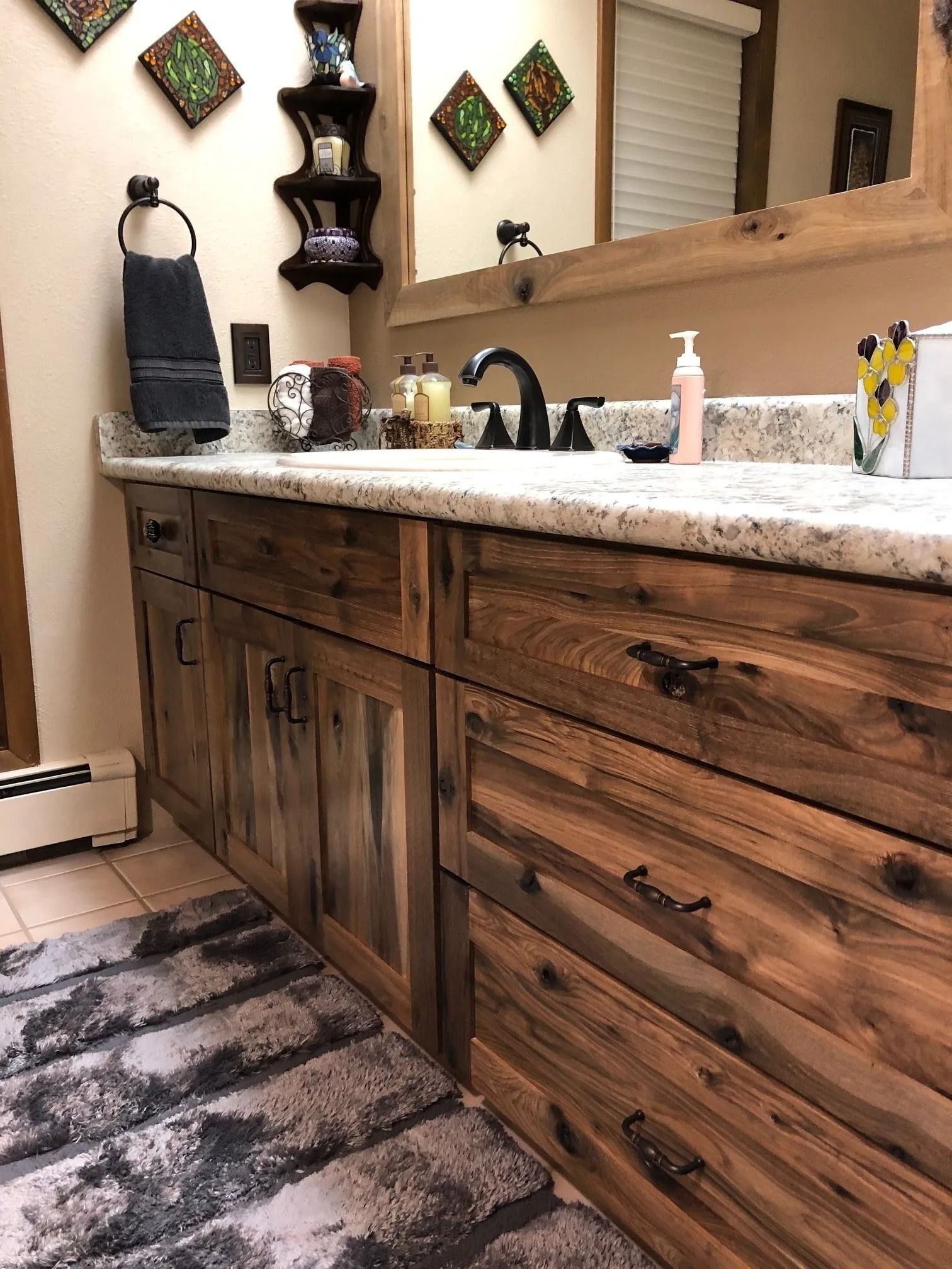 Wooden bathroom vanity with speckled countertop, sink, mirror, and decorative wall art above patterned rug.