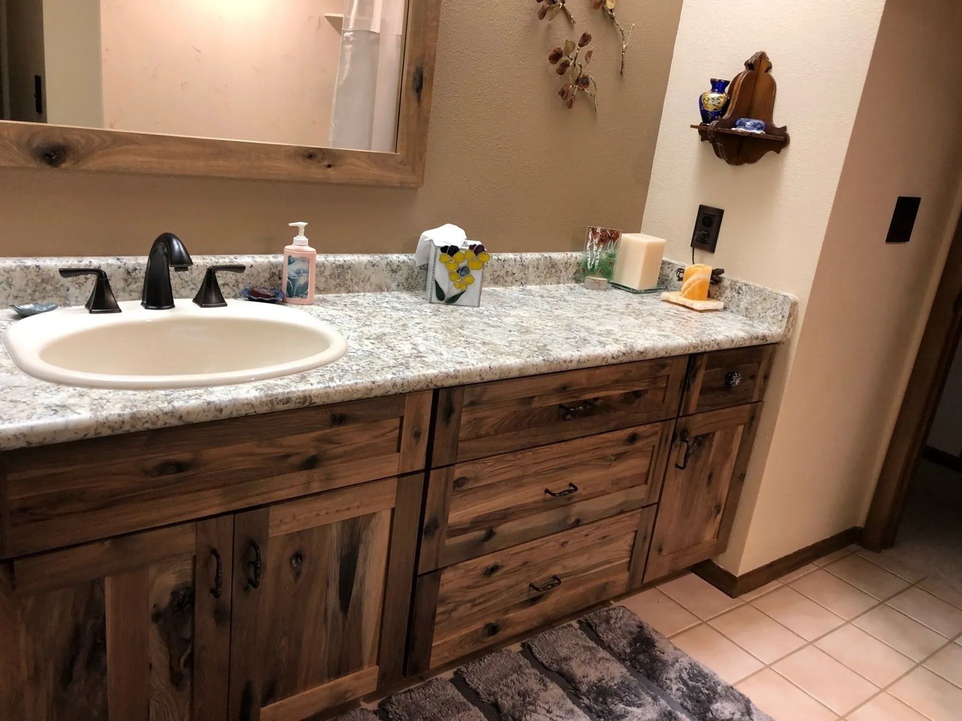 Bathroom vanity with white sink, wood cabinets, speckled countertop, mirror, and tiled floor