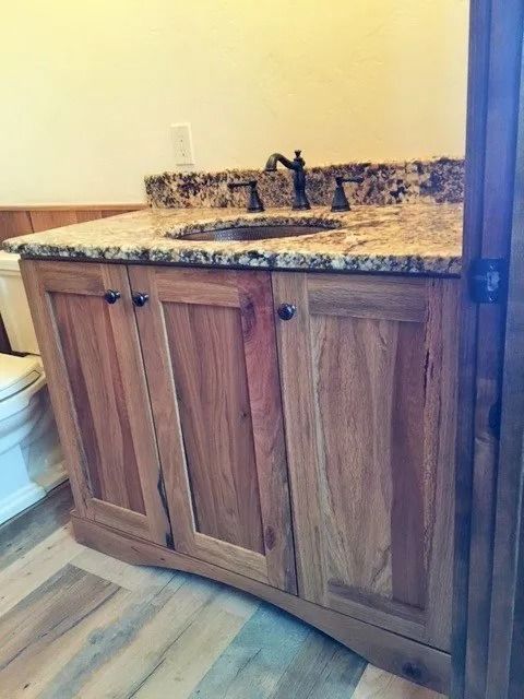Wood bathroom vanity with granite countertop and single sink against a light wall.