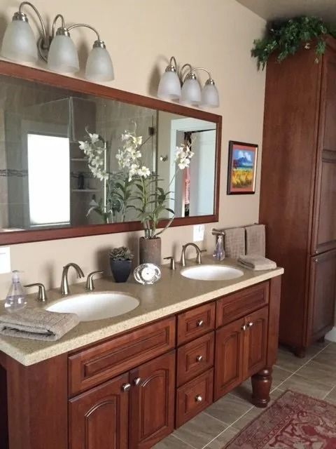 Bathroom vanity with double sinks, wood cabinets, mirror, and white wall sconces.