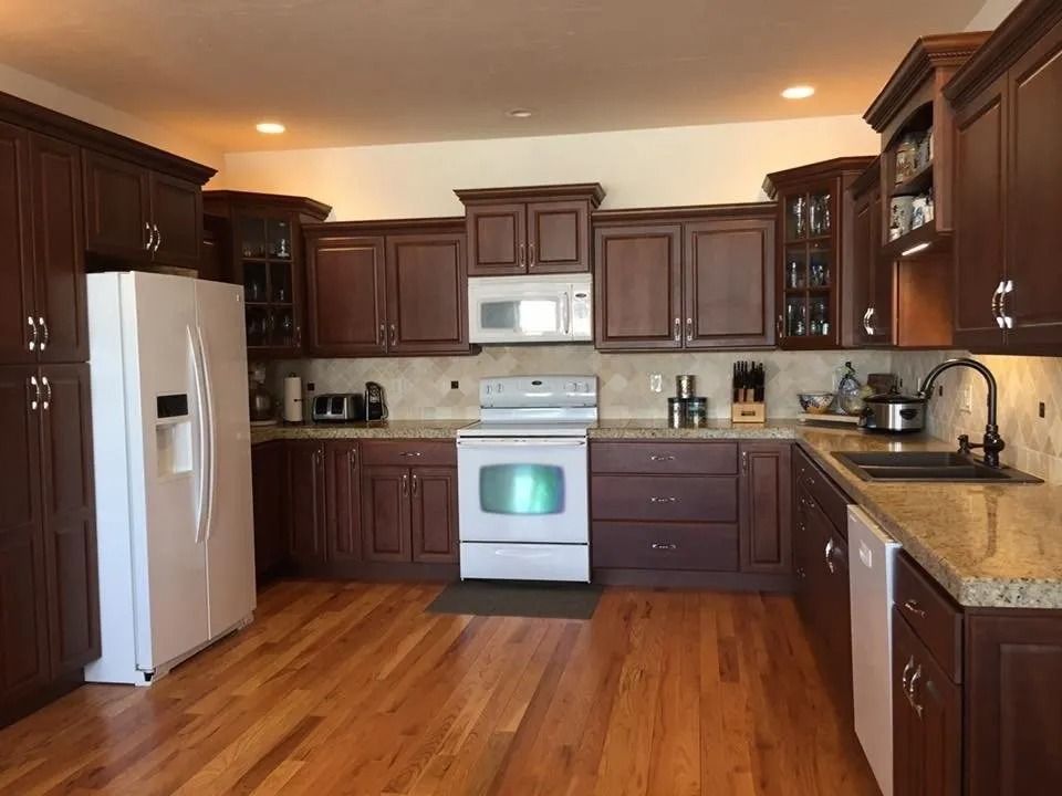 Modern kitchen with dark wood cabinets, white appliances, granite countertops, and hardwood floor