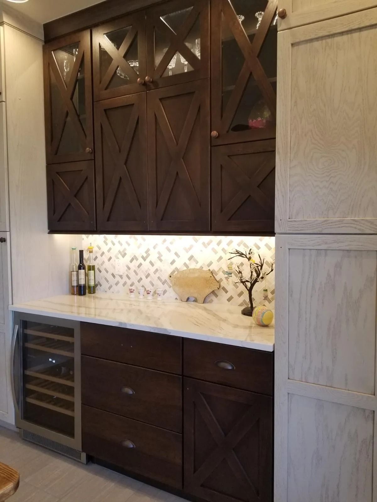 Dark wood built-in bar cabinet with wine fridge, glass backsplash, and under-cabinet lighting