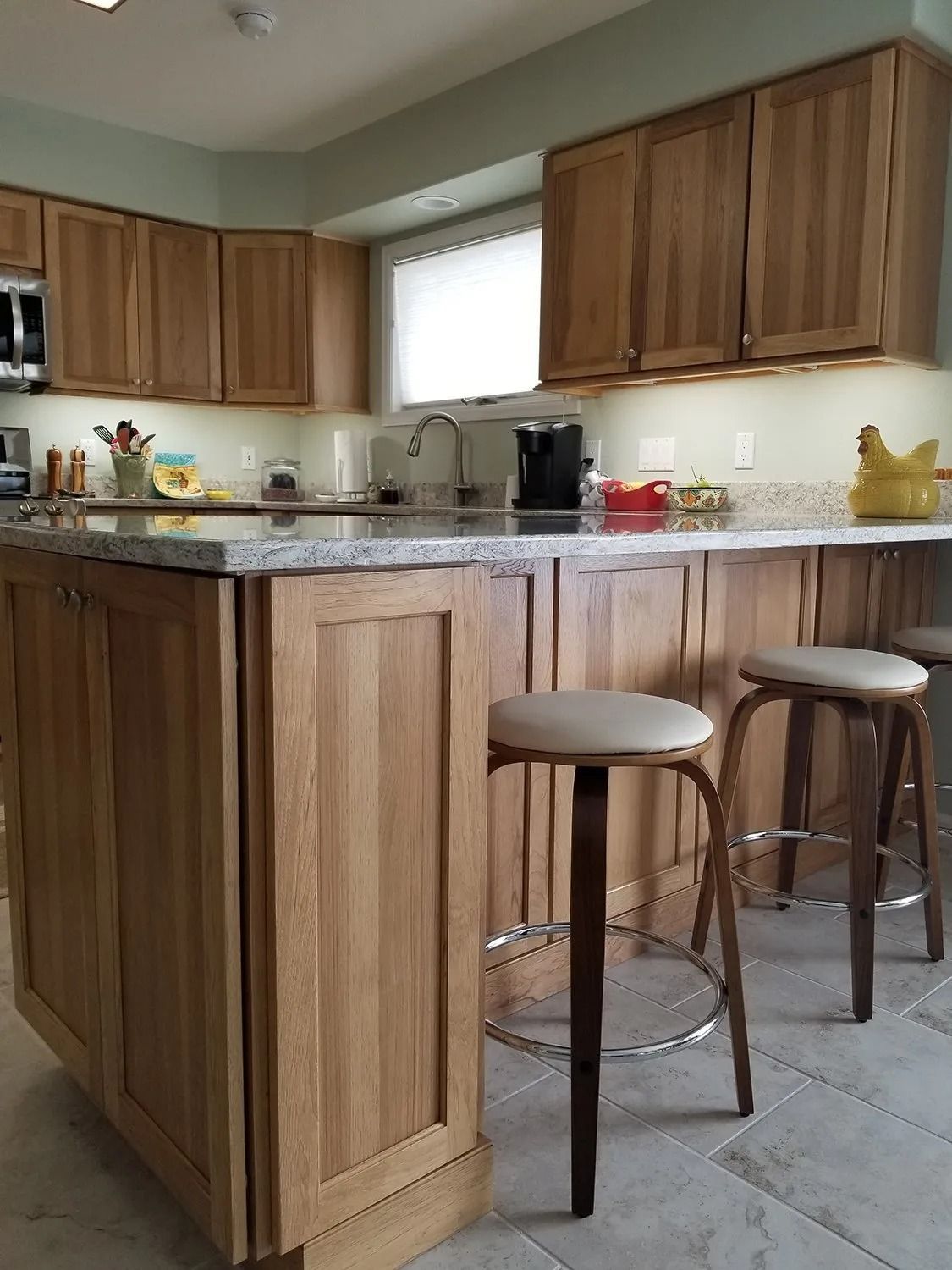 Small kitchen with wooden cabinets, granite counters, and two stools by a peninsula.