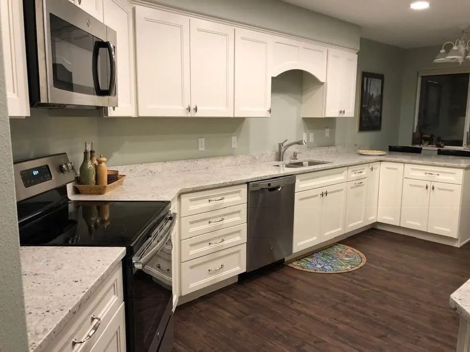 Bright modern kitchen with white cabinets, black countertops, stainless appliances, and dark wood floors