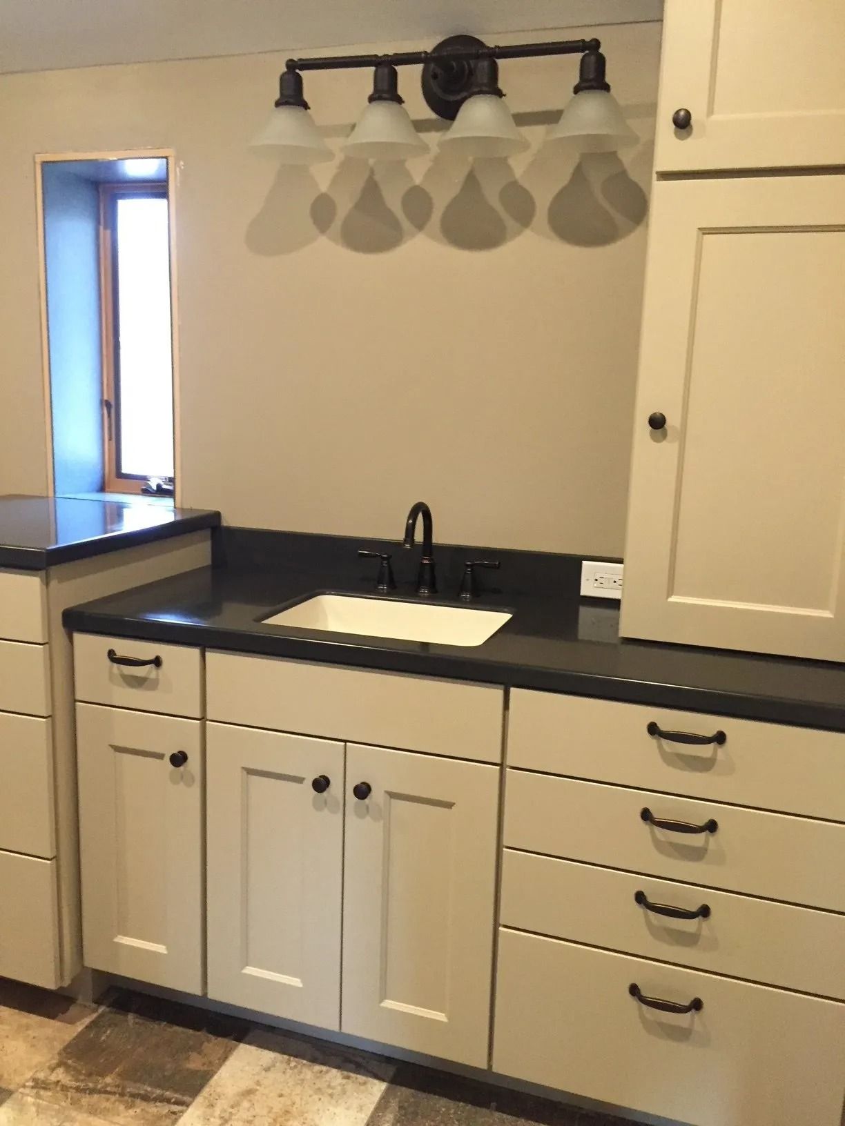 Bathroom vanity with cream cabinets, black countertop, sink, and three-bulb light fixture above mirror.