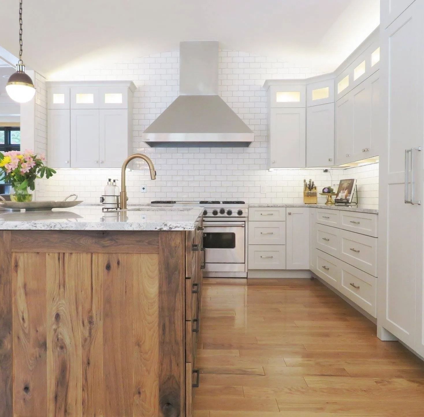 Bright white kitchen with wood island, marble counters, stainless range hood, and hardwood floors
