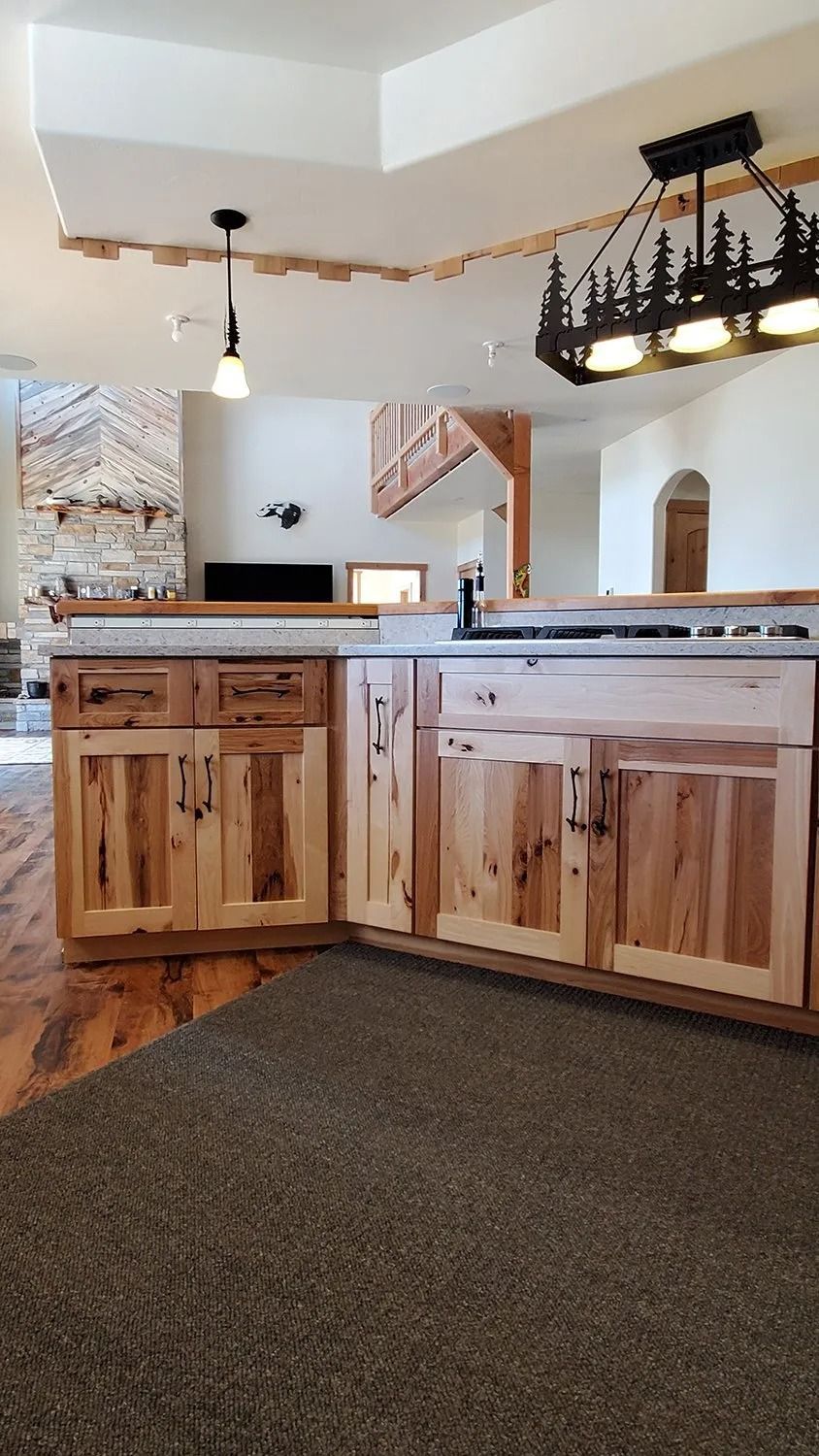 Rustic kitchen with wooden cabinets, granite counter, hanging light, and carpeted foreground