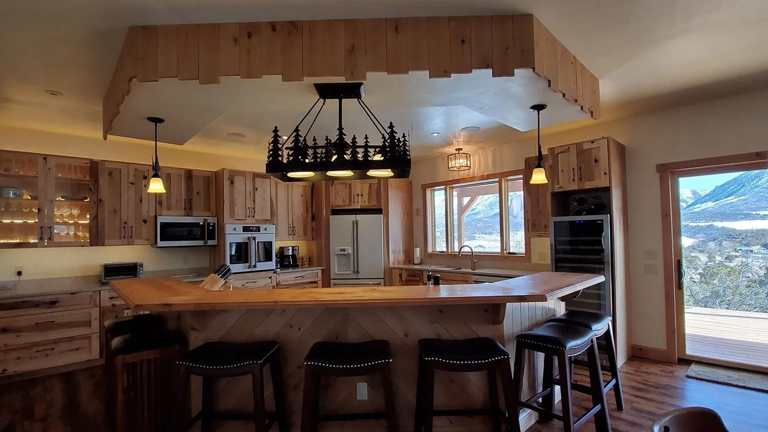 Rustic wood kitchen and dining area with island, stools, hanging light, and mountain view through windows
