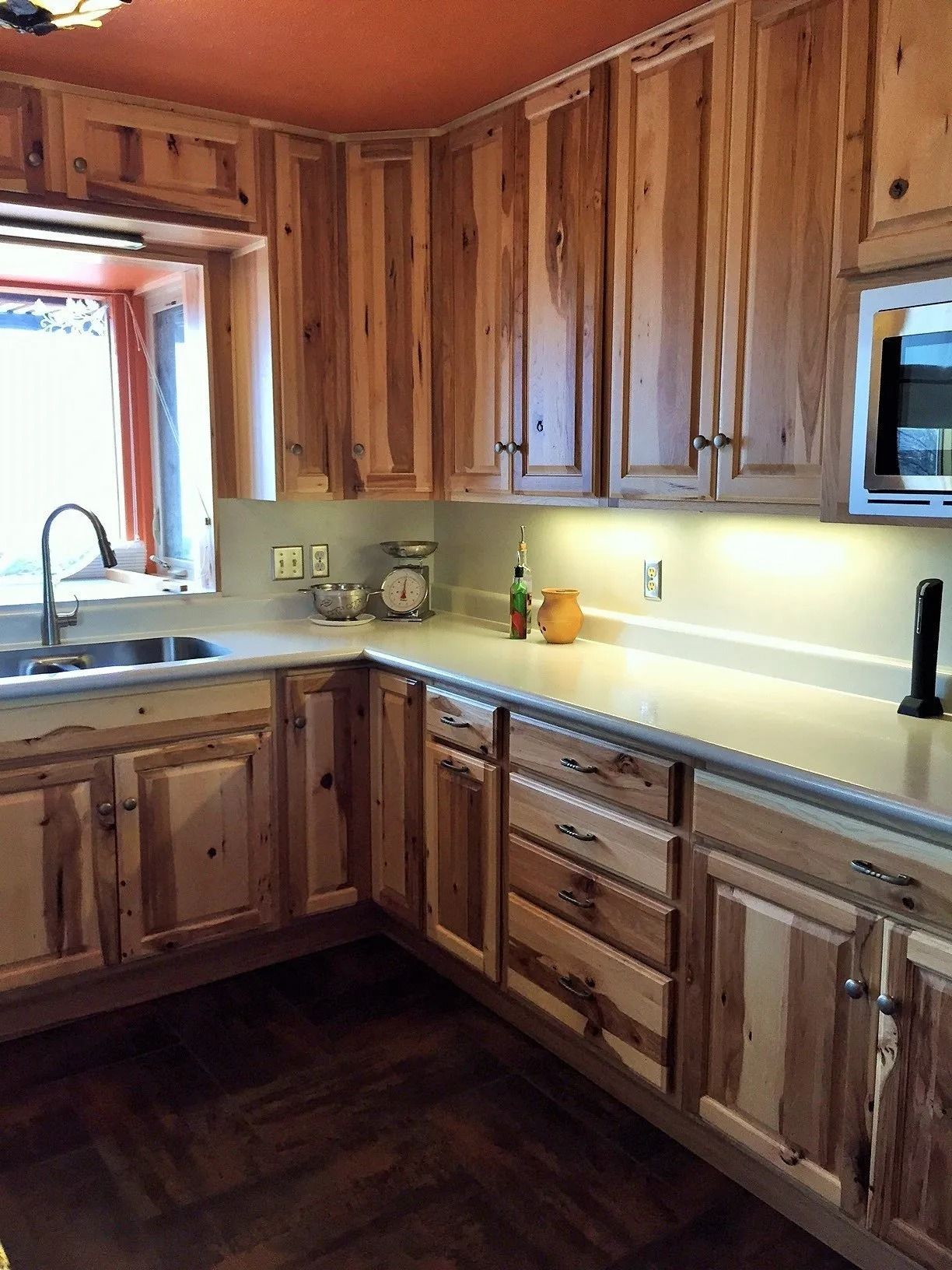Wooden kitchen with cabinets, sink by a window, and light countertop with under-cabinet lighting