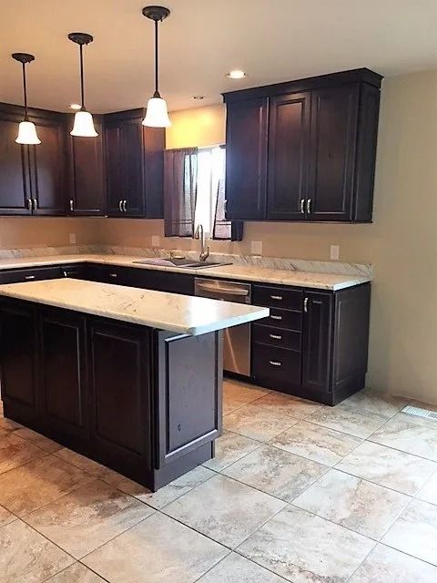 Modern kitchen with dark wood cabinets, black island, beige countertops, and tiled floor