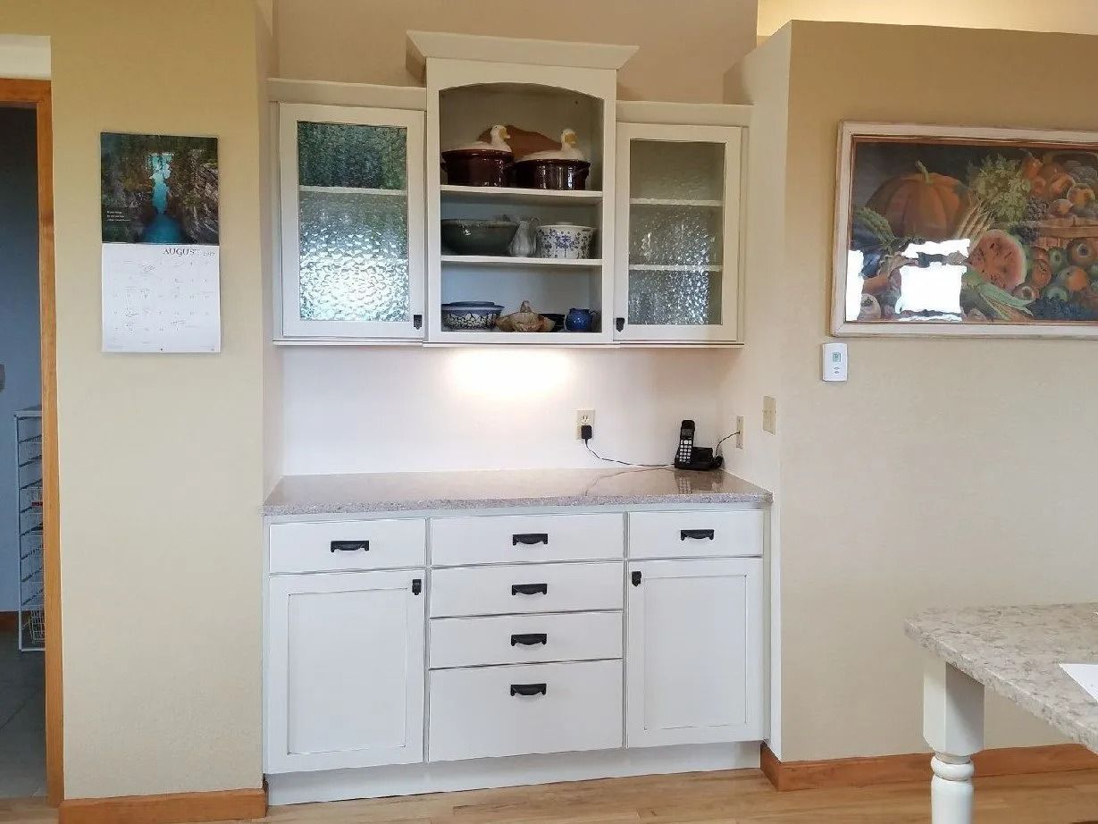 Kitchen nook with white cabinets, frosted glass doors, beige walls, and a framed landscape on the right.