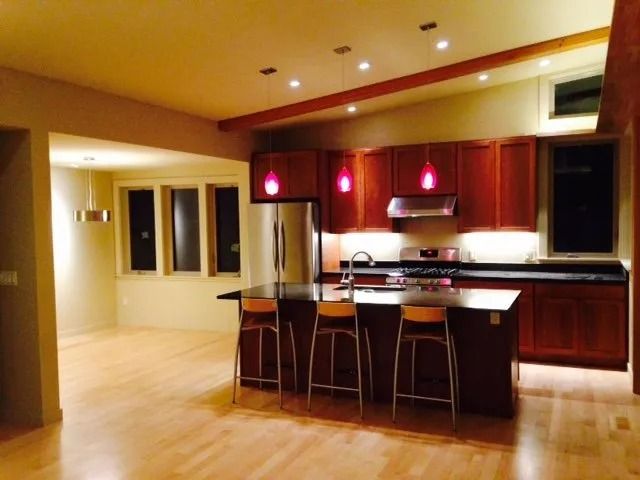Modern kitchen with dark wood cabinets, island seating, and red pendant lights in an open floor plan.