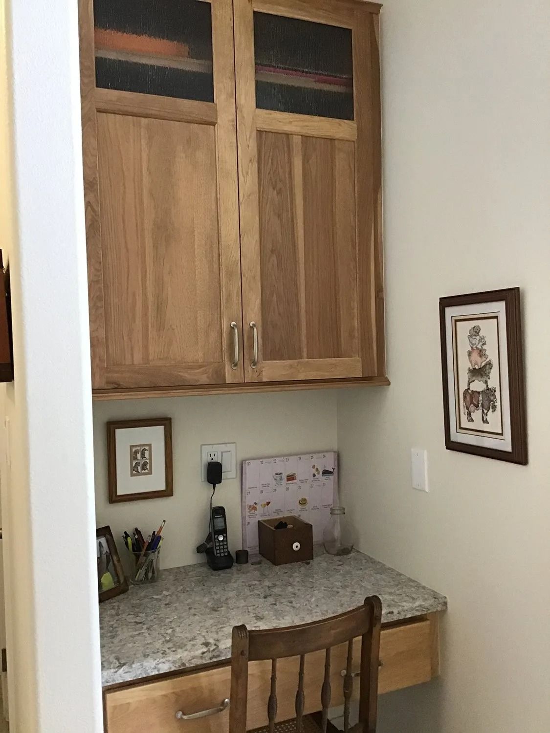 Small home office nook with wooden cabinets, granite desk, and a chair against a beige wall.