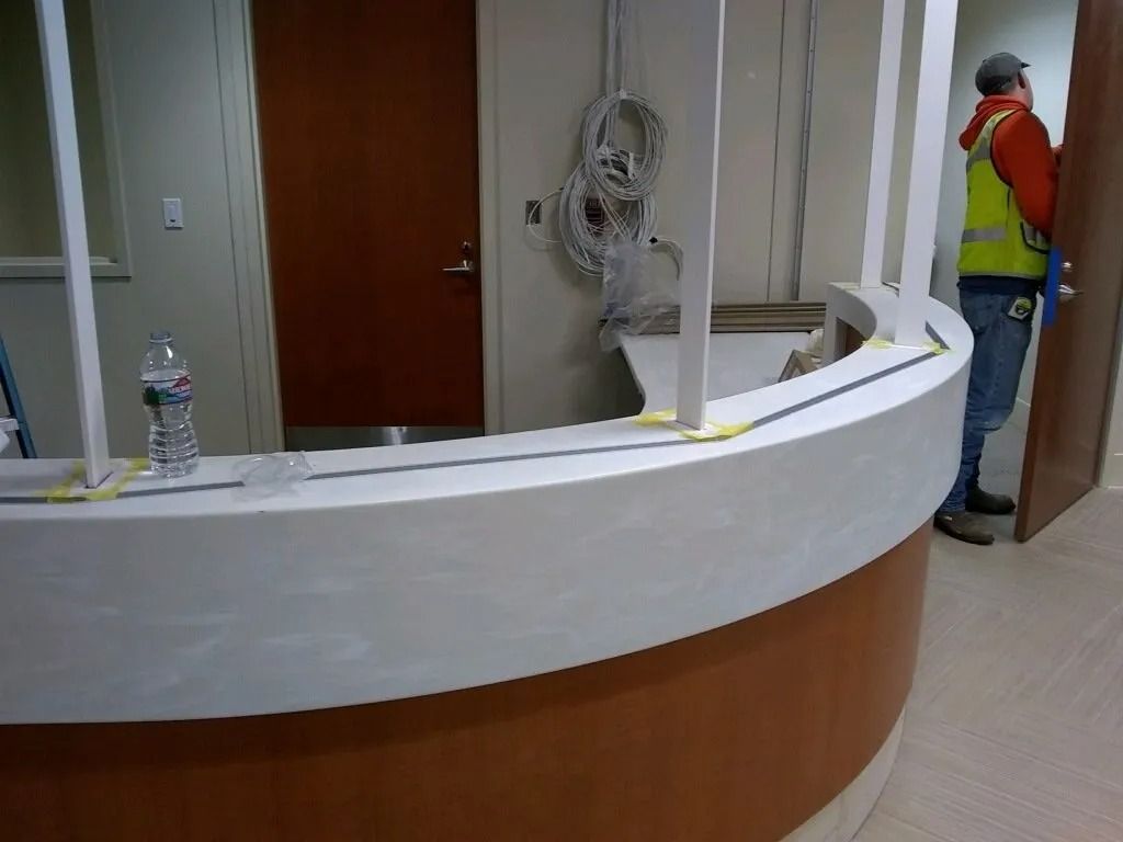 Curved reception desk in an office lobby with a worker in an orange vest standing at the right.