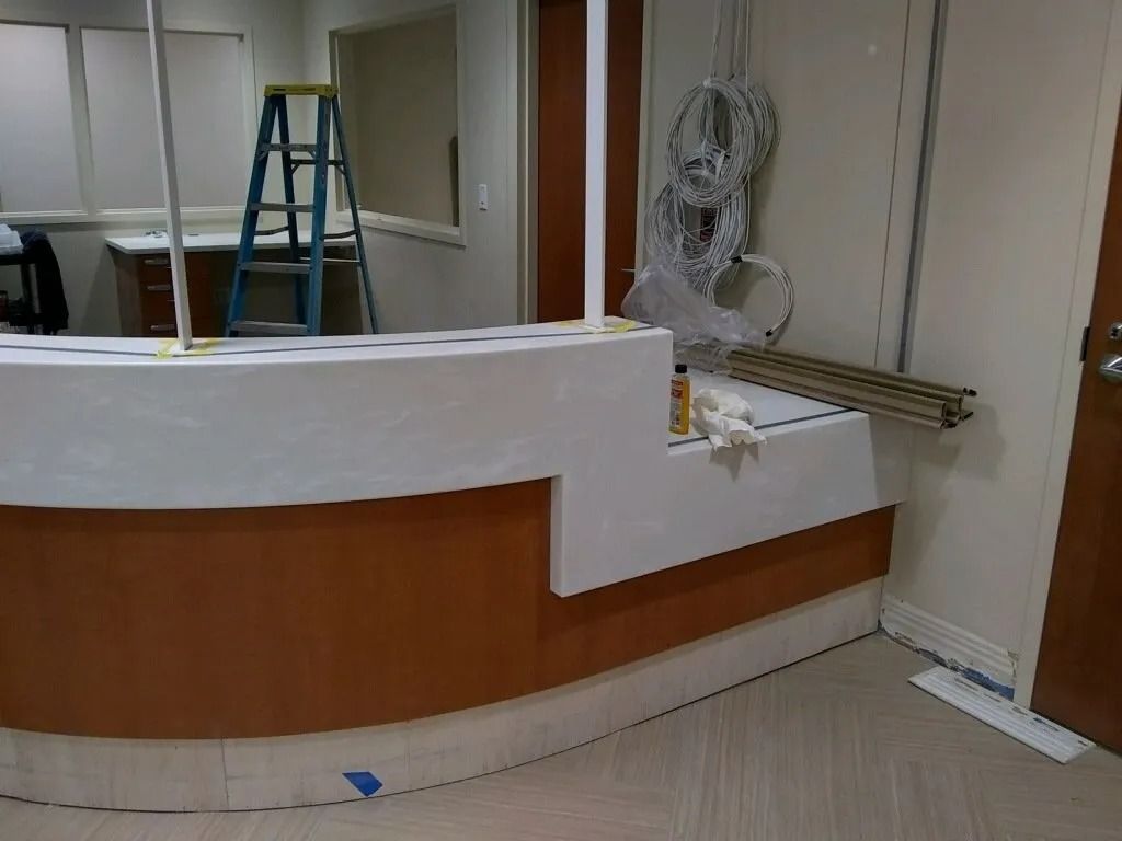 Empty reception desk in a room under renovation, with a blue ladder and wall fan visible.