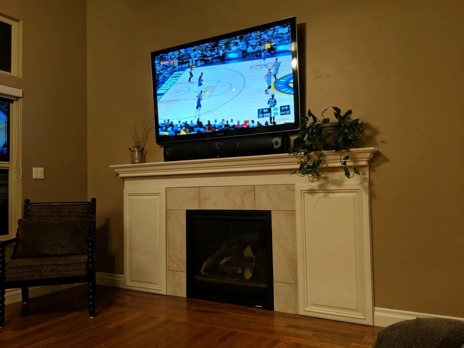 Living room with TV on a white fireplace mantel above a dark fireplace, beige walls and wooden chair.
