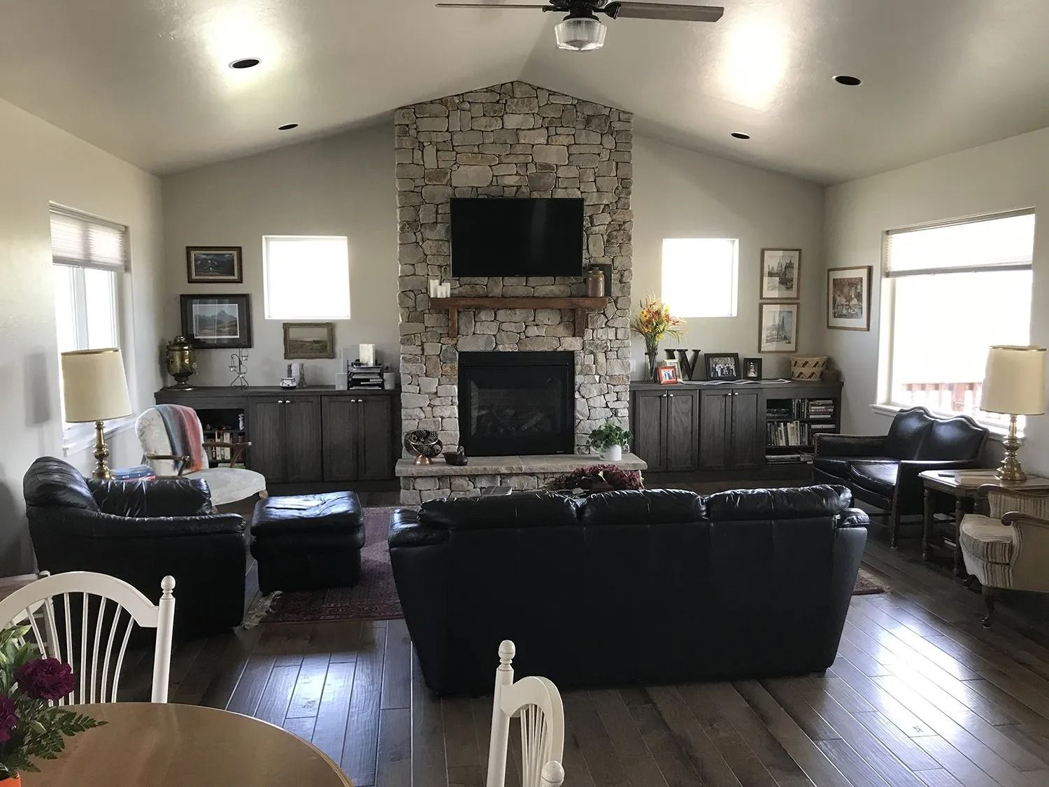 Spacious living room with stone fireplace, black sofas, white walls, and large windows