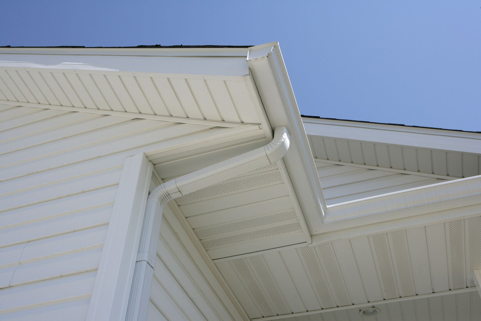 White house exterior with siding and gutters against a blue sky.