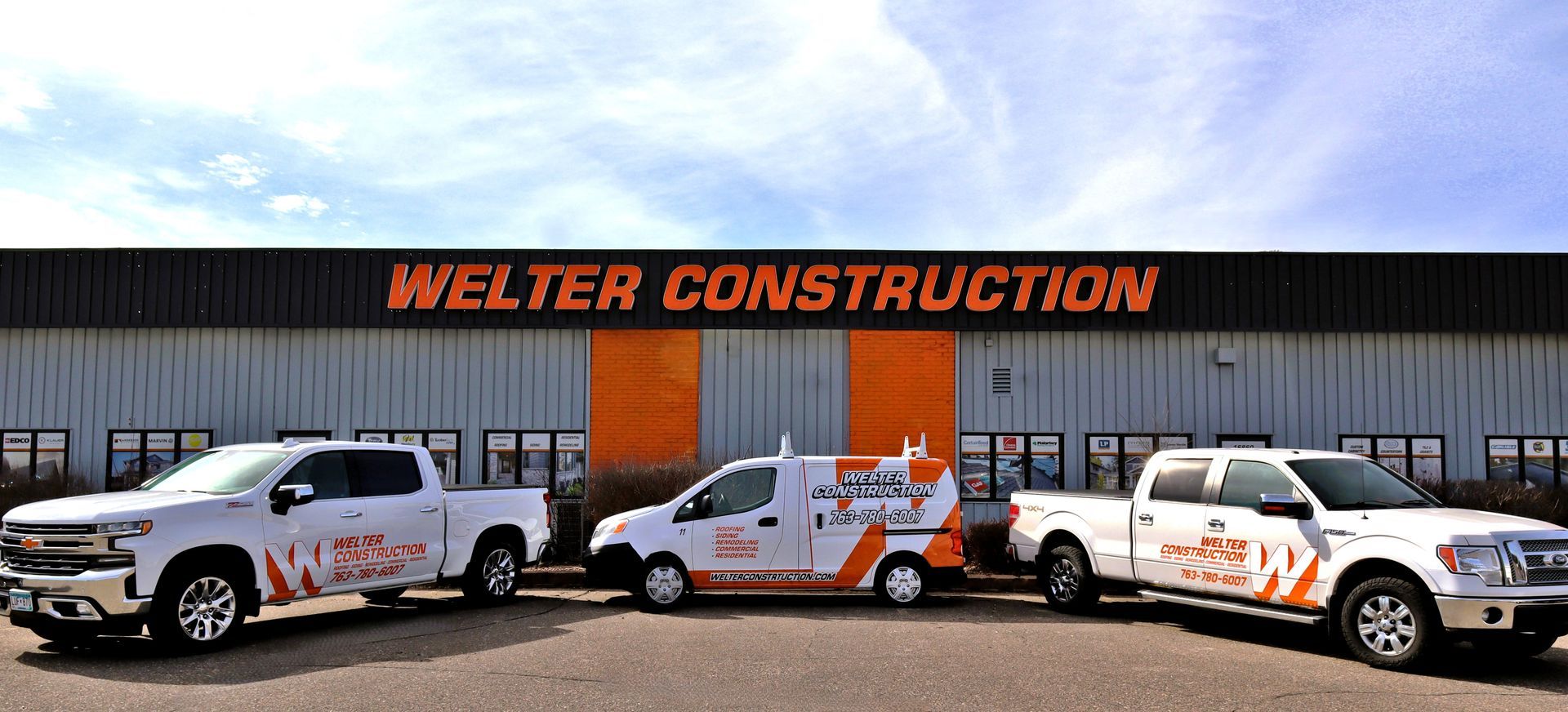 Three white Welter Construction vehicles parked in front of building with orange logo.