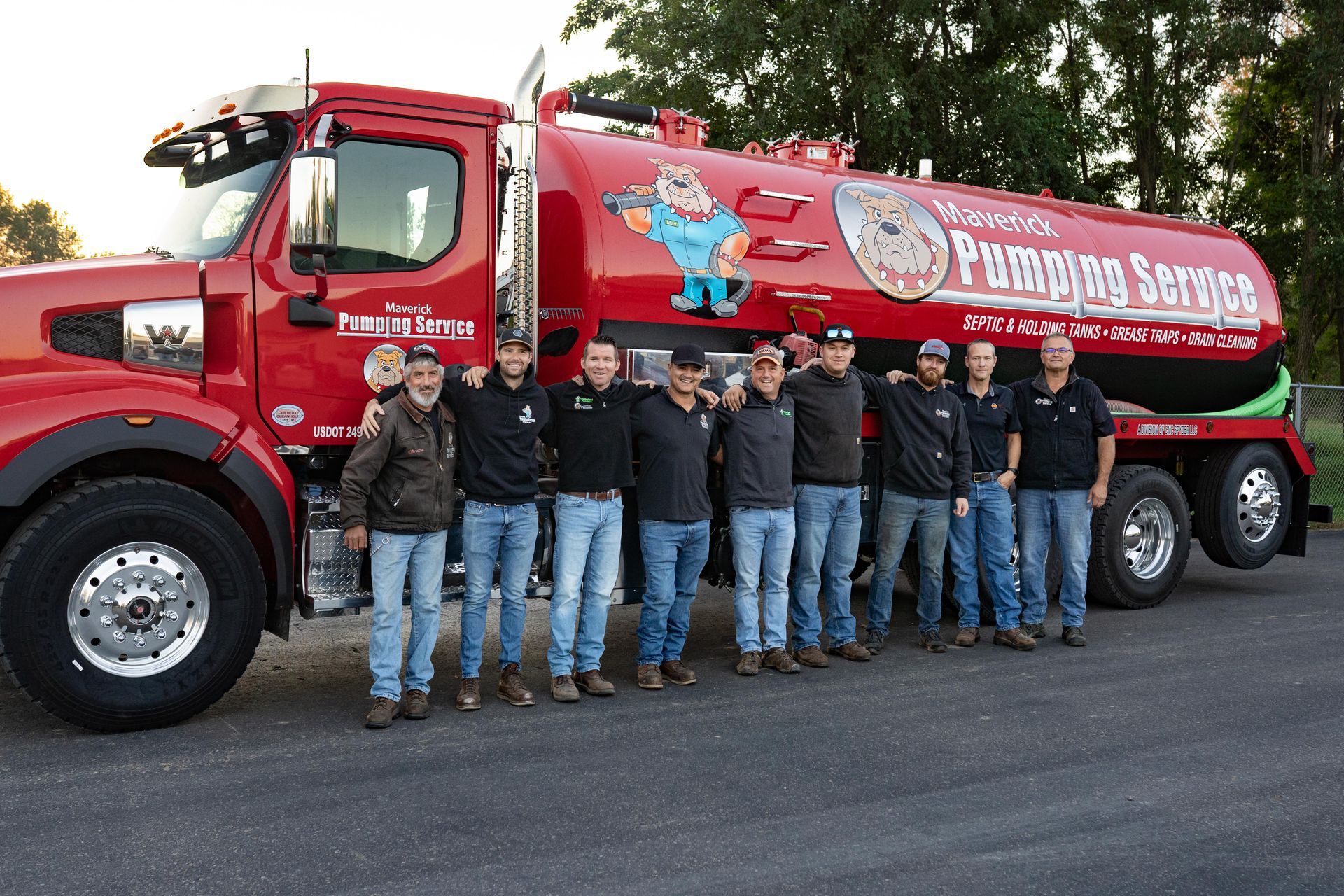 Group of people standing beside a red fuel tanker truck on a street, posing for a photo