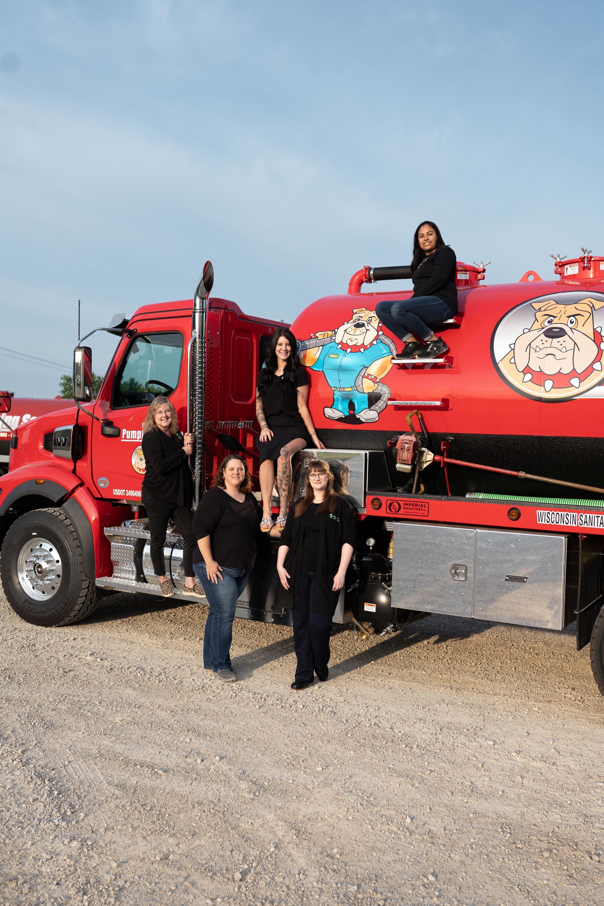 Five people posing by a red fire truck in a gravel lot under a clear sky