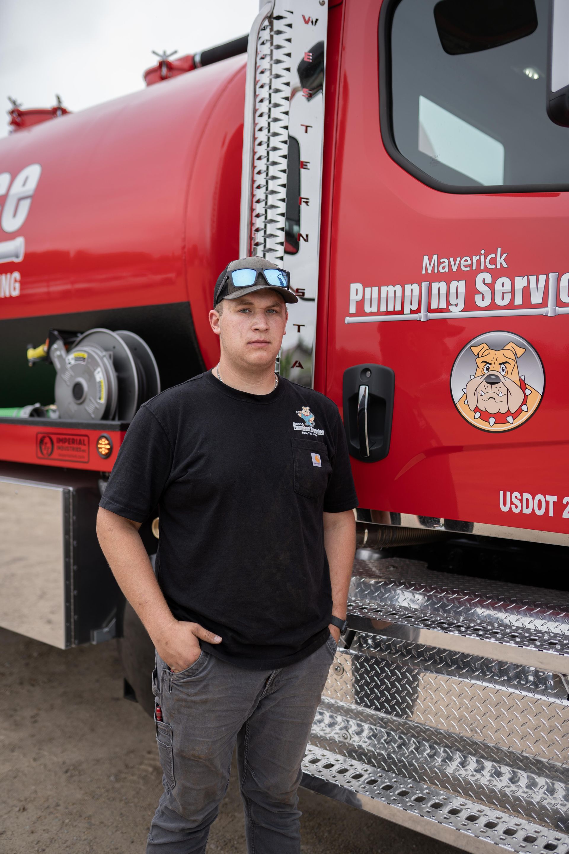 Man standing beside a red Maverick Pumping Service truck, wearing a black shirt and cap.