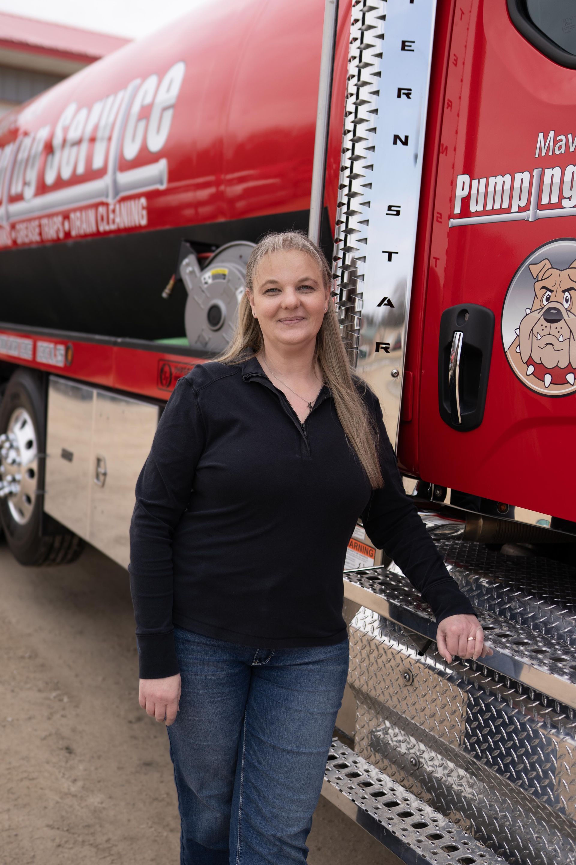 Woman standing beside a red tanker truck, smiling near the front steps.
