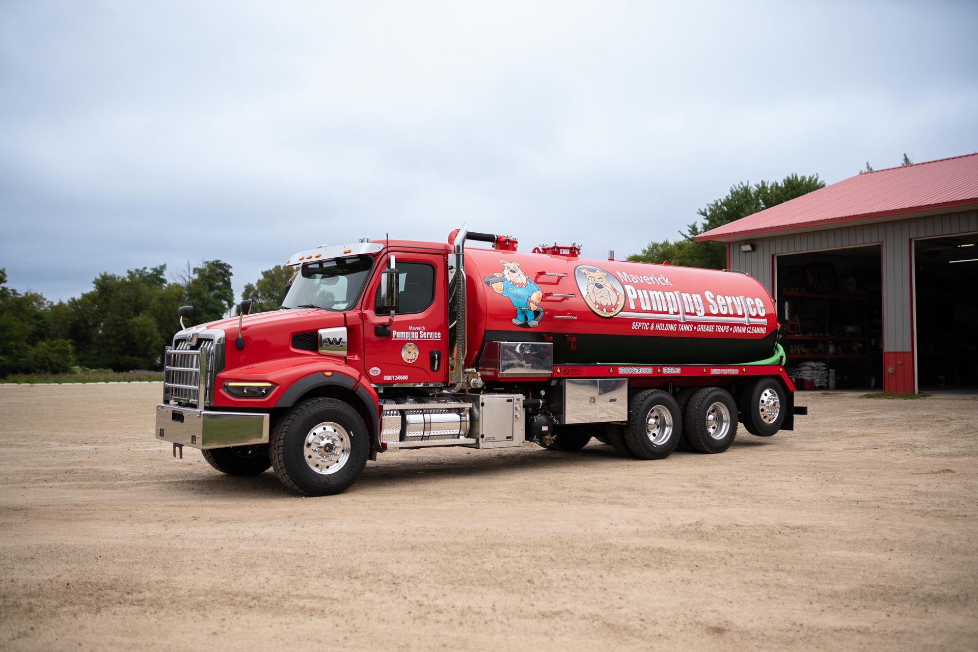 Red fuel tanker truck parked on a gravel lot beside a building.