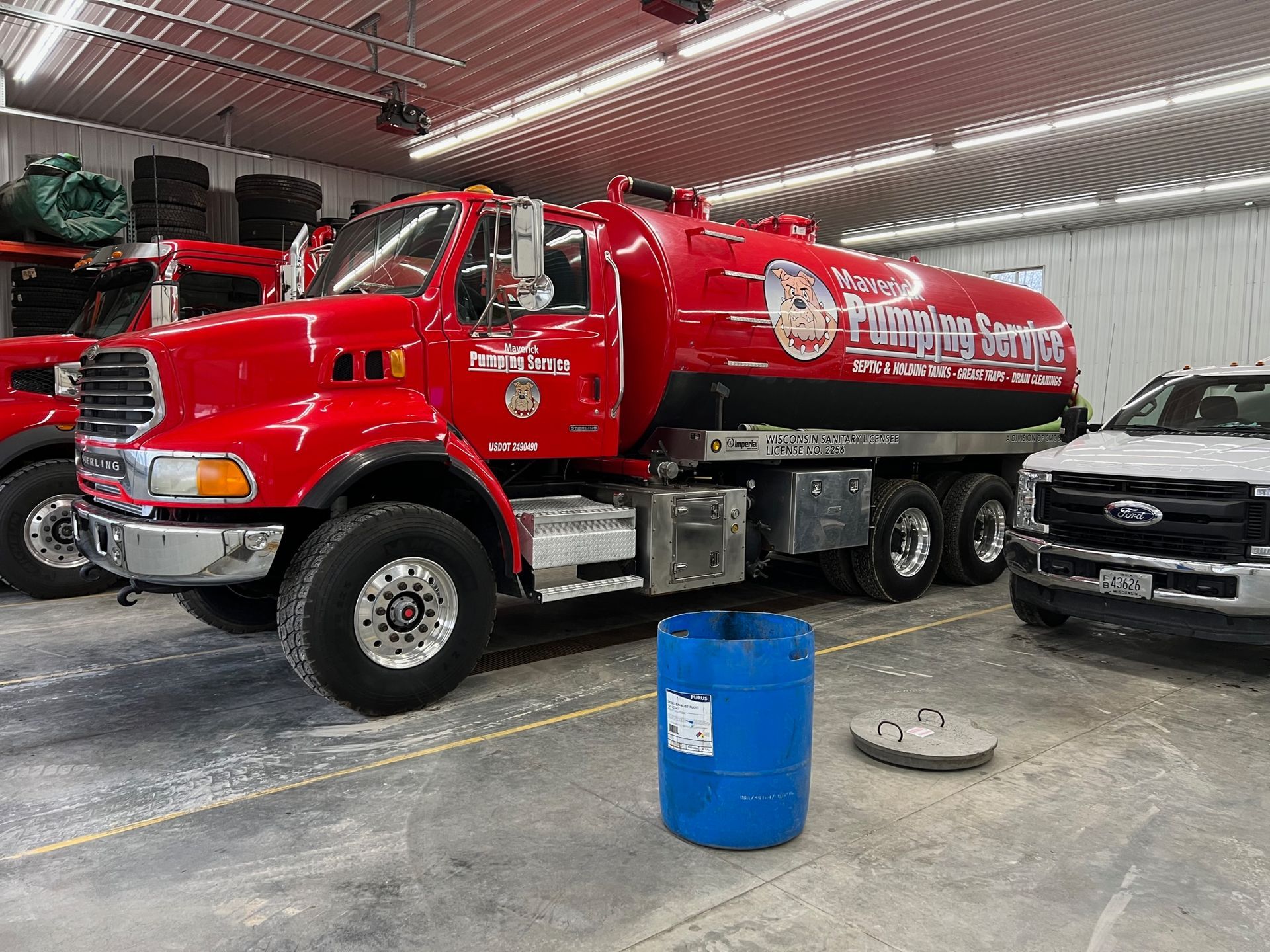 Red tanker truck in an indoor garage with a blue barrel in front of it