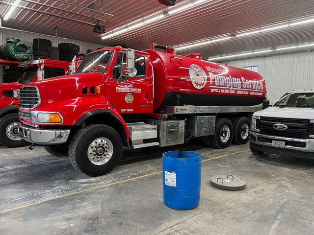 Red fire tanker truck parked inside a garage beside a white pickup truck and a blue barrel