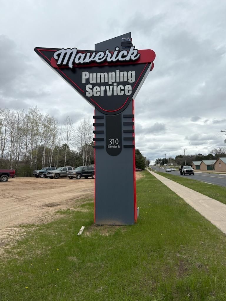 Maverick Pumping Service roadside sign on a grassy verge under a cloudy sky