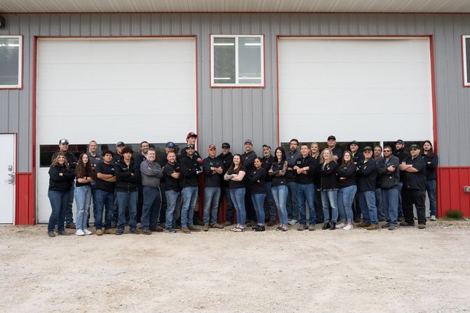Group of people in dark uniforms standing in front of a large gray garage building