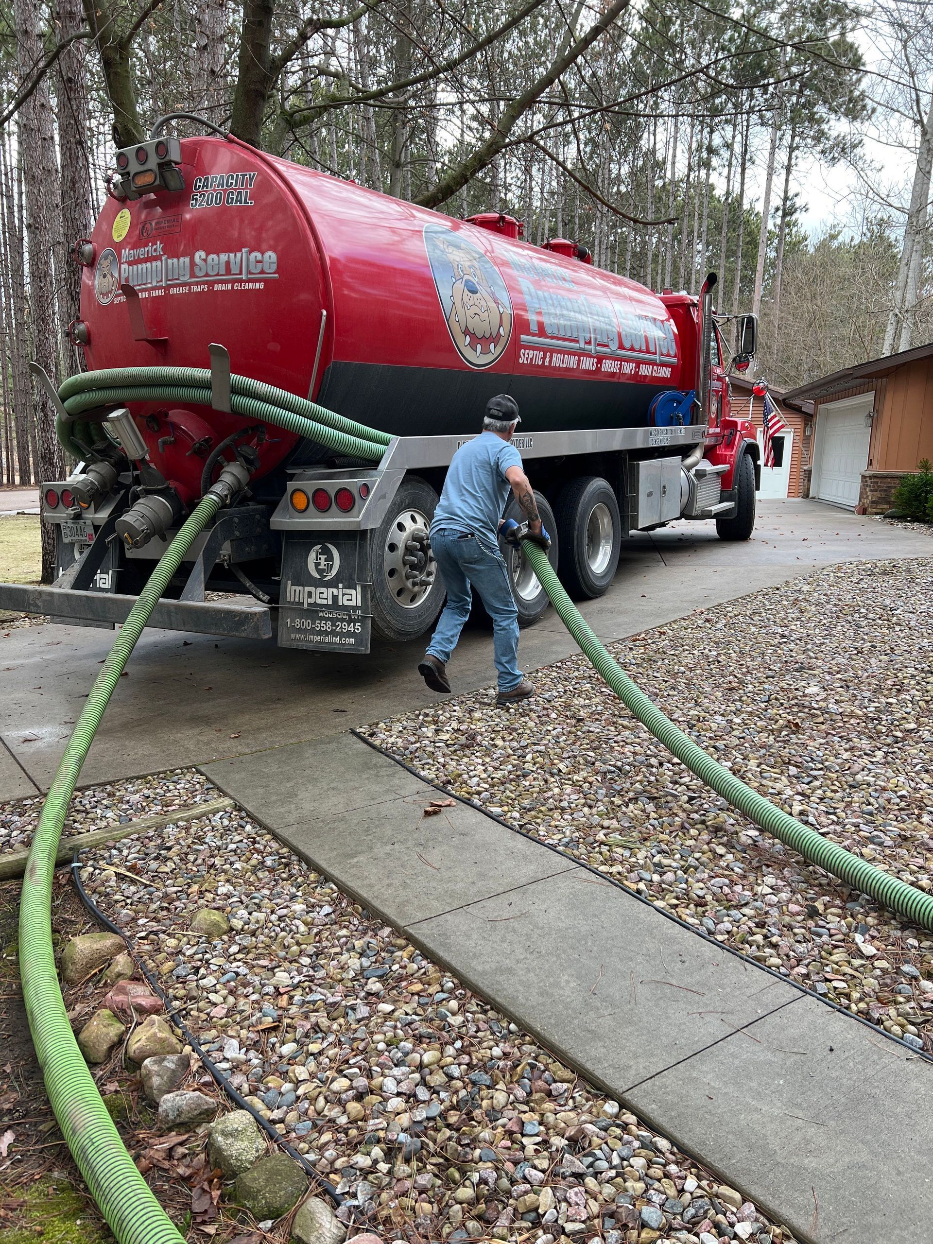 Red water tanker truck with hoses being used in a wooded driveway.
