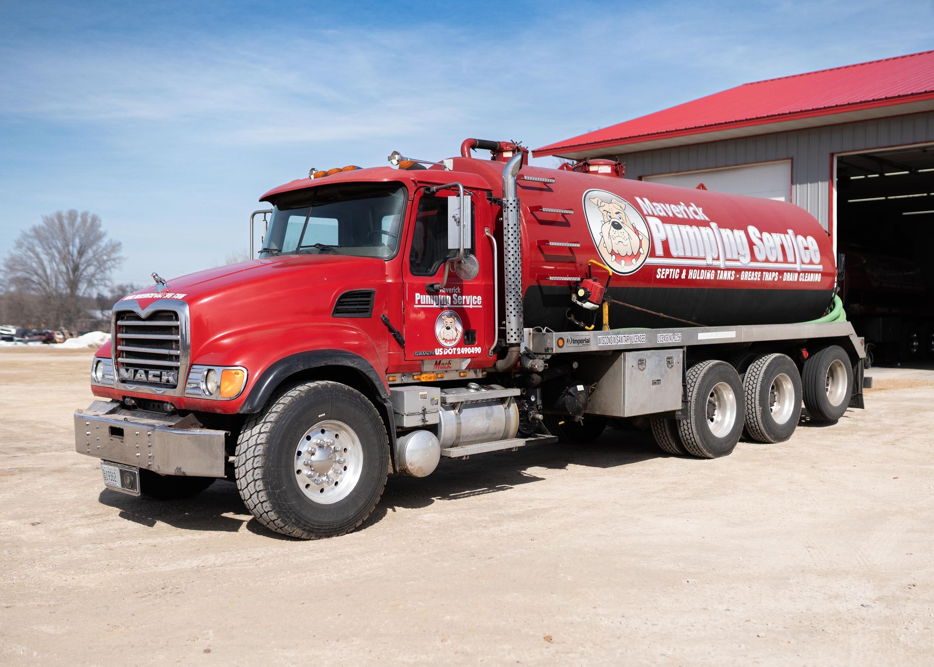 Red fuel tanker truck parked beside a red garage on a sunny day