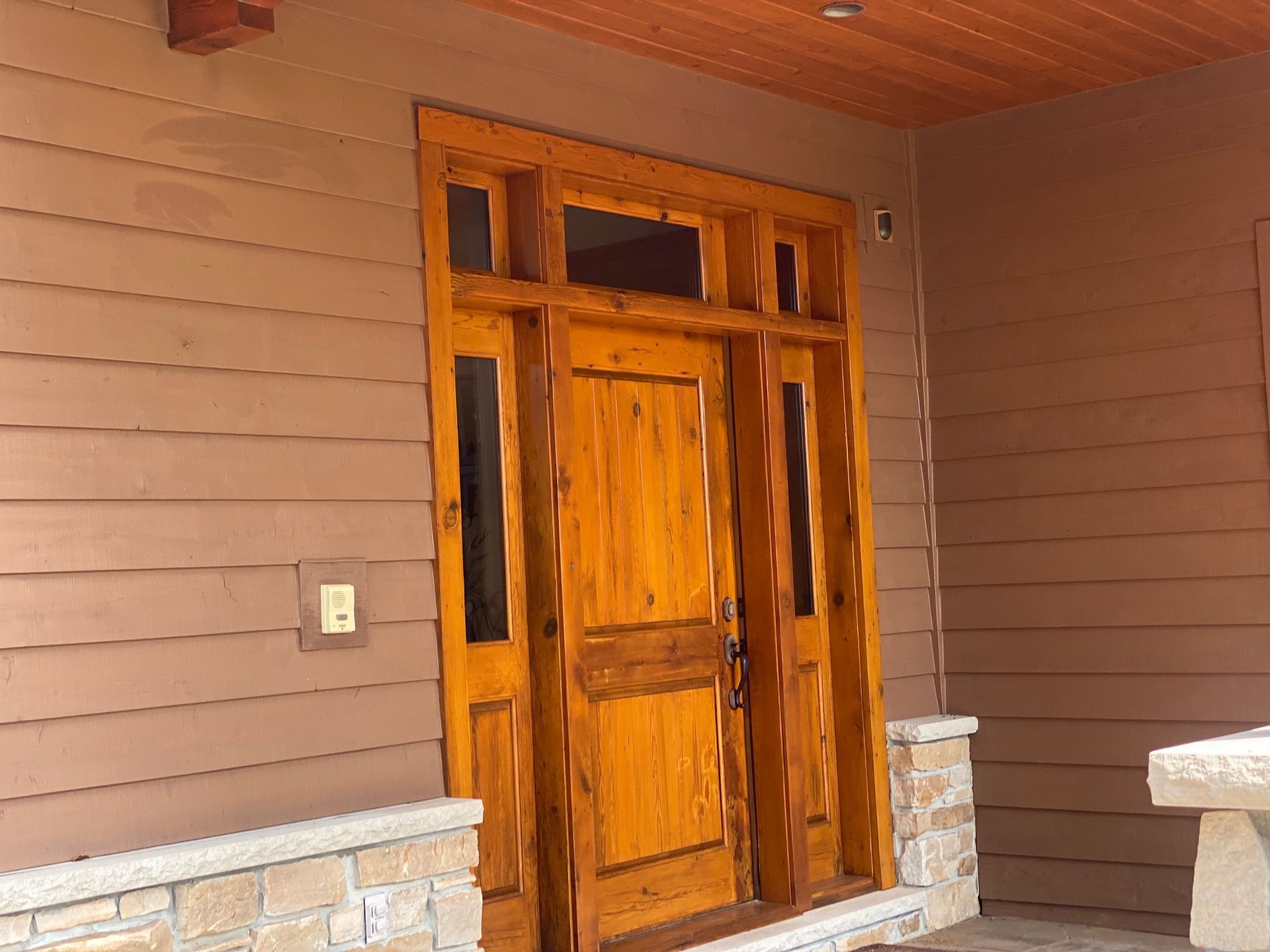 A wooden door is sitting on a porch next to a stone wall.
